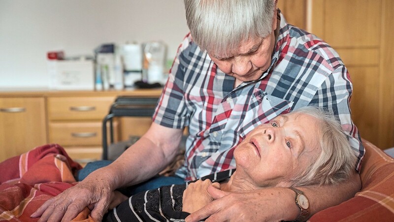 Ein pflegender Ehemann nimmt in seiner Wohnung seine an Demenz und Parkinson erkrankte Ehefrau in den Arm. Der Pflegestützpunkt Landshut und die Koordinierungsstelle Demenz sind Anlaufstellen für Fragen.