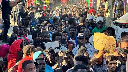 Migranten warten in einer Schlange auf Grundnahrungsmittel, die von Mitarbeitern des Roten Kreuzes und der Organisation „Sur Sur“ verteilt werden. Migranten warten in einer Schlange auf Grundnahrungsmittel, die von Mitarbeitern des Roten Kreuzes und der Organisation „Sur Sur“ verteilt werden.