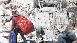 Ein Mann läuft mit seinen Habseligkeiten über Erdbebentrümmer in Antakya. Ein Mann läuft mit seinen Habseligkeiten über Erdbebentrümmer in Antakya.