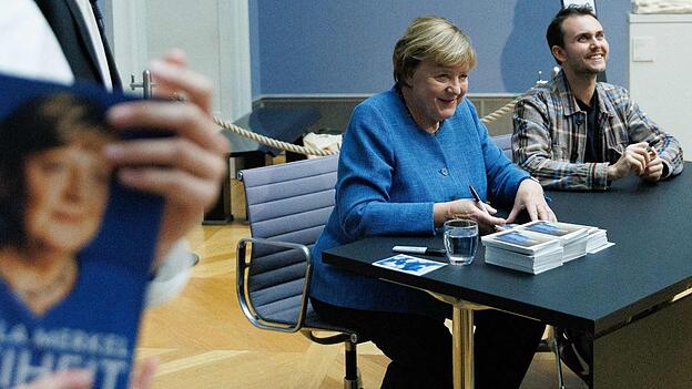 Merkel signiert Kunstpostkarten im Bode-Museum neben dem Maler ihres dort ausgestellten Porträts, Jérémie Queyras. Merkel signiert Kunstpostkarten im Bode-Museum neben dem Maler ihres dort ausgestellten Porträts, Jérémie Queyras.