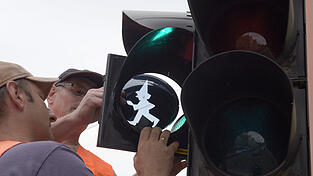 Mitarbeiter des Tiefbauamts montieren 2017 in Augsburg an einer Fußgängerampel die Silhouette des Kasperl. Mitarbeiter des Tiefbauamts montieren 2017 in Augsburg an einer Fußgängerampel die Silhouette des Kasperl.